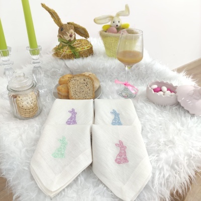 guardanapos brancos com coelhos coloridos sobre mesa felpuda com pão, velas, biscoitos e coelhos decorativos