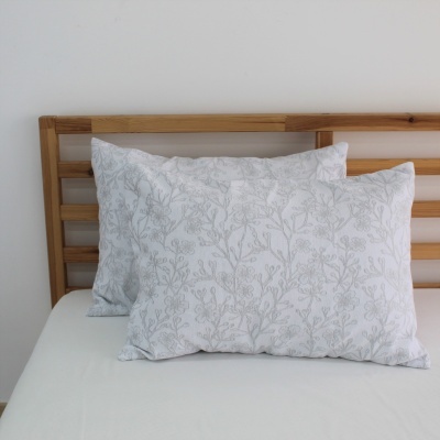 Frontal de par de fronhas brancas com padrão floral cinza claro sobre cama com lençol branco e cabeceira de madeira