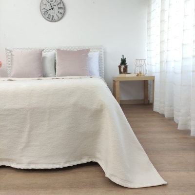 Cama com colcha branca, almofadas rosa e branca, relógio e mesa de cabeceira com vaso e objeto decorativo
