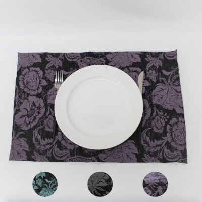 Jogo americano de tecido com padrão floral em preto e roxo, prato branco, garfo e faca