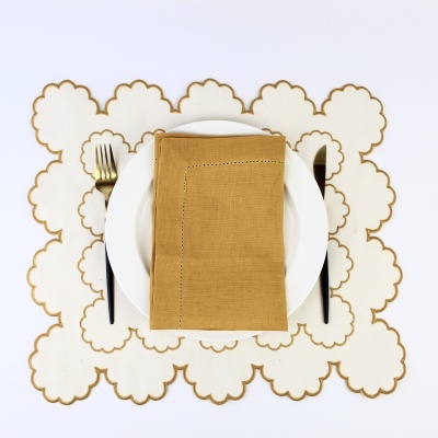 Mesa posta com prato branco, guardanapo castanho, talheres dourados e pretos e placemats brancos com bordas castanhas