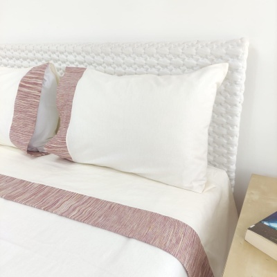 Cama com almofadas e lençóis brancos com detalhes rosa e cabeceira trançada branca