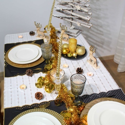 Mesa natalícia com decoração em dourado, branco e preto, incluindo pratos, copos, velas e enfeites de rena e árvore
