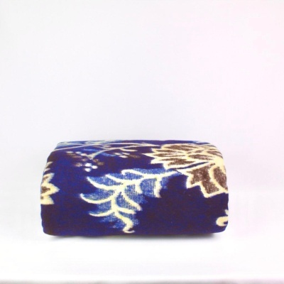 Cobertor azul com padrão floral bege e branco dobrado sobre superfície branca