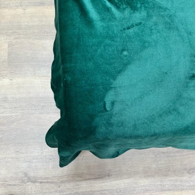 Almofada verde de veludo numa superfície de madeira clara
