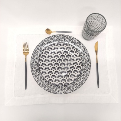 Conjunto de jantar com pratos brancos e pretos, talheres dourados e copo transparente