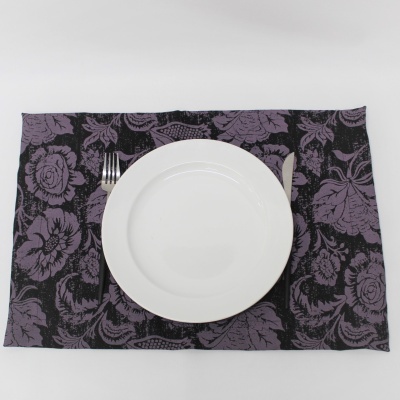 Jogo americano preto com flores roxas, prato branco, garfo e faca