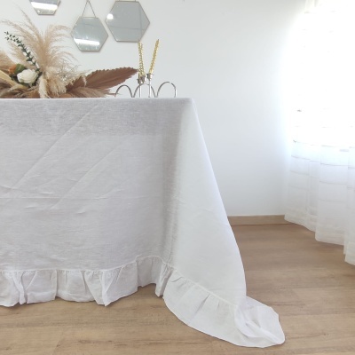 Toalha de mesa branca com babados em ambiente iluminado com arranjo floral e espelhos hexagonais