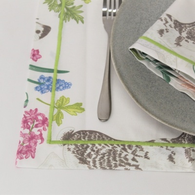 Mesa posta com guardanapos e toalha de mesa com padrão floral, prato cinza e garfo de metal