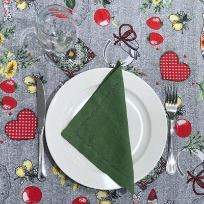 Mesa posta com toalha de mesa cinza estampada com girassóis, corações e maçãs, prato branco, guardanapo verde, talheres e copo.