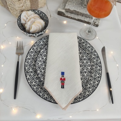 Mesa posta com prato preto e branco, guardanapo bordado, talheres pretos, bowl com pão e copo com bebida laranja