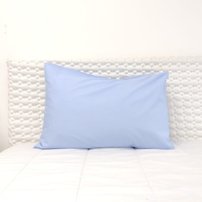Almofada azul claro sobre cama com cabeceira branca acolchoada.