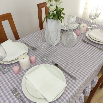 Mesa posta com toalha lilás e branca, pratos, copos e velas