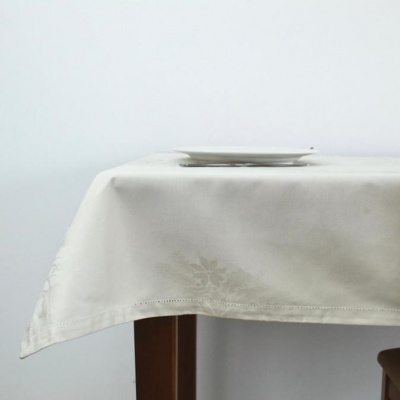 Toalha de mesa branca com padrão floral e prato branco sobre mesa de madeira.