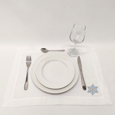 Conjunto de mesa com individual branco bordado, pratos brancos, talheres prateados e copo de vinho.
