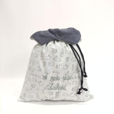 Saco de tecido branco com padrões de coelhos e texto bordado verde, fecho com cordão preto
