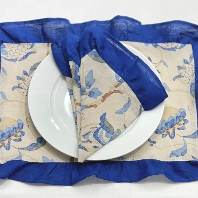 Individuais e guardanapo em tecido com padrão floral azul e castanho, bordo azul forte, com prato branco