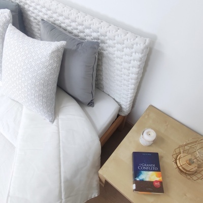 Cama com cabeceira trançada branca e mesa de cabeceira com livro e vela
