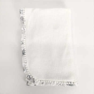 Toalha branca com borda floral cinza e pompons brancos.