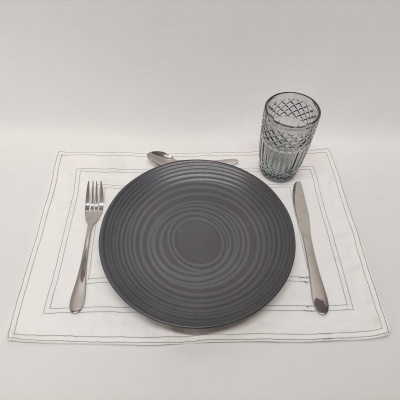 Conjunto posto de mesa com prato cinzento, talheres metálicos, copo de vidro texturizado e toalhete branco