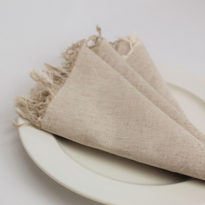 Guardanapo bege de tecido com franjas sobre prato branco