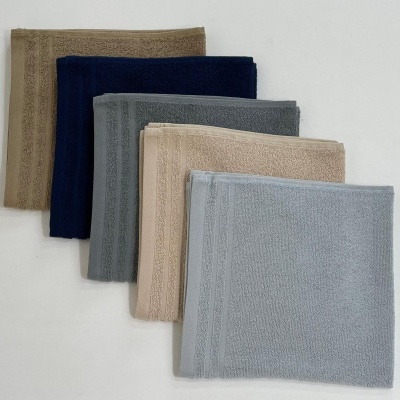 Cinco toalhas de mão dobradas em várias cores com padrão decorativo nas bordas