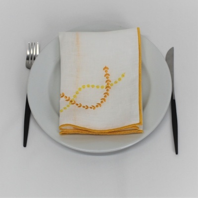 Jogo americano com prato branco, talheres pretos e guardanapo branco bordado a amarelo.
