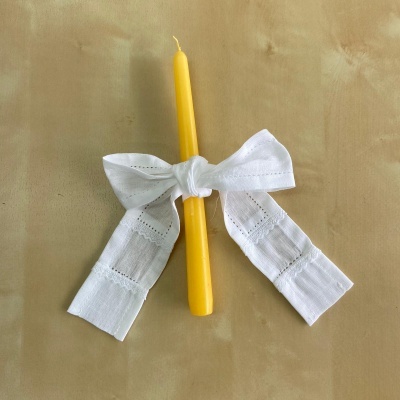 Vela amarela com laço branco bordado sobre fundo bege.