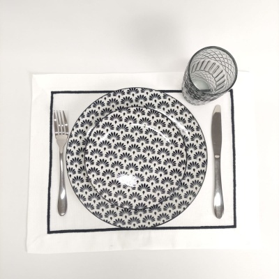 Conjunto de pratos, talheres e copo sobre individual branco com borda preta