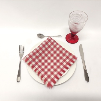Conjunto de loiça com prato branco, guardanapo vermelho e branco, talheres metálicos e copo com base vermelha