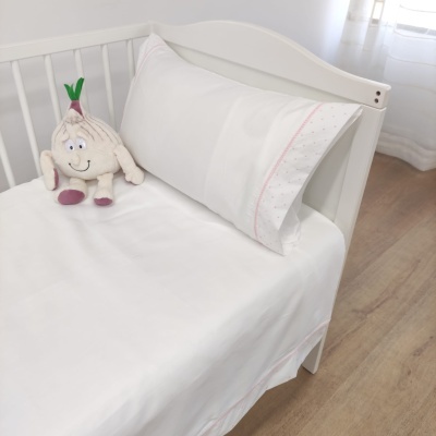 Cama de criança branca com lençóis brancos com detalhes rosa e brinquedo de tecido branco