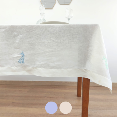 Toalha de mesa branca com bordados de coelhos coloridos em mesa de madeira.