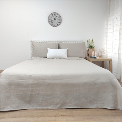 Cama de casal com colcha e almofadas cinza clara e branca em quarto minimalista com relógio e mesa de madeira ao lado