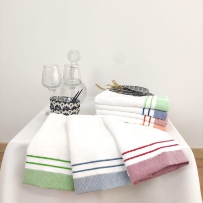 Toalhas brancas com riscas coloridas sobre mesa branca com copos e decantador de vidro