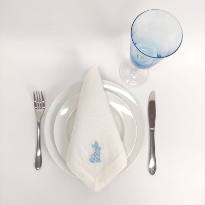 Conjunto de prato branco com guardanapo bordado de coelho azul, talheres metálicos e copo azul