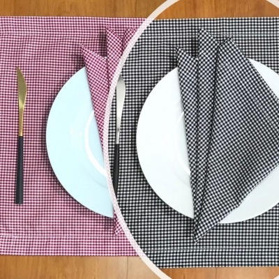 Mesa posta com toalhas e guardanapos xadrez em rosa e preto com pratos e talheres sobre uma superfície de madeira