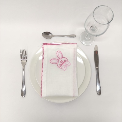 Conjunto de prato branco com guardanapo bordado rosa, talheres metálicos e copo de vidro