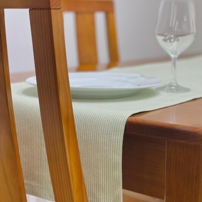 Conjunto de mesa de jantar de madeira com toalha bege, prato branco e copo de vinho.