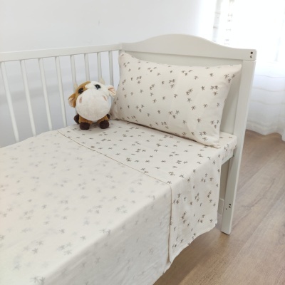 Roupa de cama bege com padrão floral para berço, almofada e peluche numa cama branca