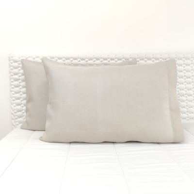 Dois almofadas retangulares bege numa cama branca com cabeceira branca texturizada