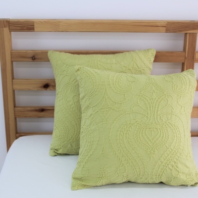 Duas almofadas decorativas verde claro com padrão texturizado sobre cama de madeira