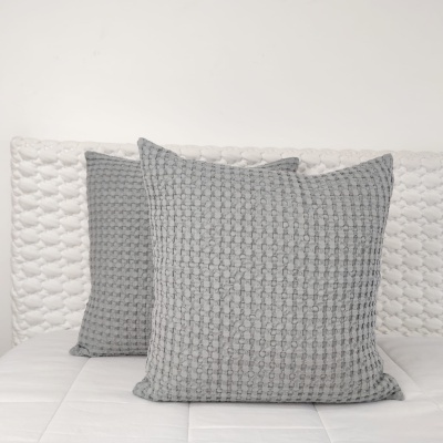 Duas almofadas cinzentas texturizadas numa cama branca com cabeceira texturizada