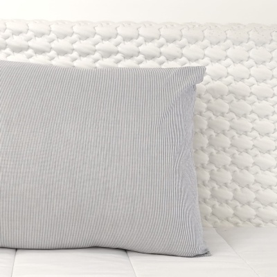 Almofada cinzenta com riscas finas brancas numa cama com colcha branca e cabeceira acolchoada com padrão de losangos.