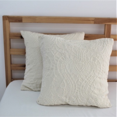 Duas almofadas creme com padrão texturizado em cima de cama branca com cabeceira de madeira