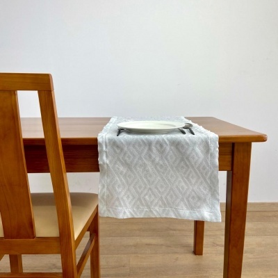 Mesa de madeira com toalha branca, prato e talheres, cadeira ao lado.