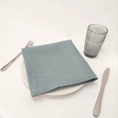 Conjunto de mesa com prato branco, guardanapo azul, talheres metálicos e copo de vidro transparente