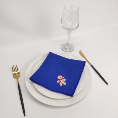 Conjunto de louça branca com guardanapo azul bordado com boneco de gengibre, talheres e copo