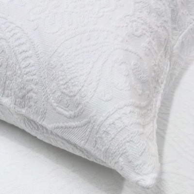 Almofada branca texturizada com padrão bordado sobre tecido branco.
