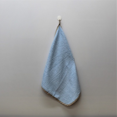 Toalha azul claro pendurada com bordas bege numa parede cinzento claro