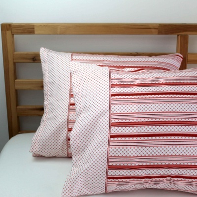 Duas almofadas brancas com padrões vermelhos sobre cama com estrado de madeira